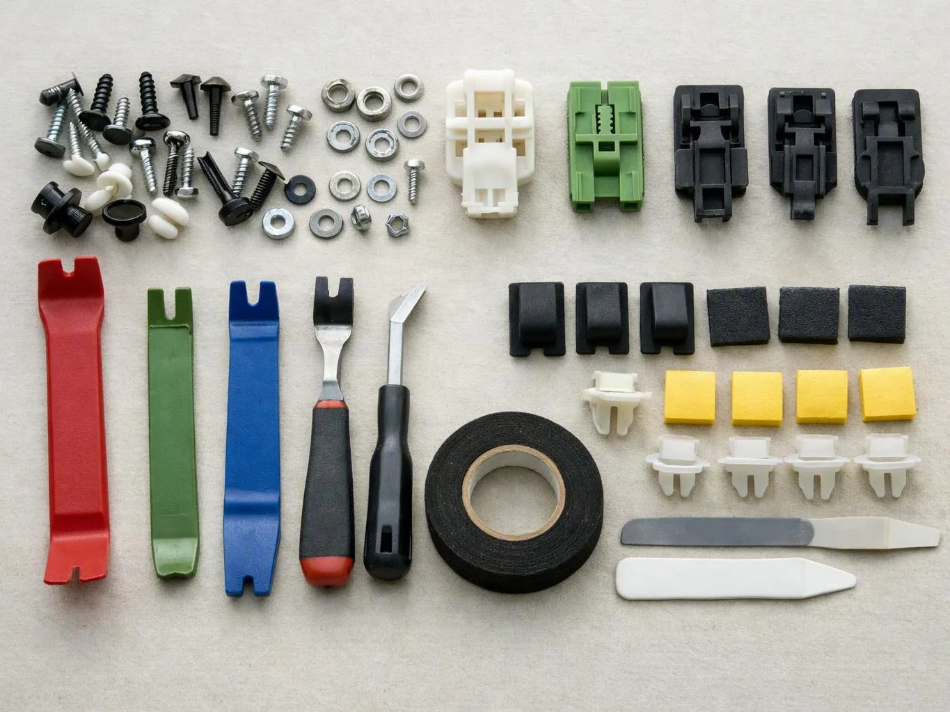 Assorted screws, clips, trim tools, foam pads, and tape are laid out neatly on a light surface
