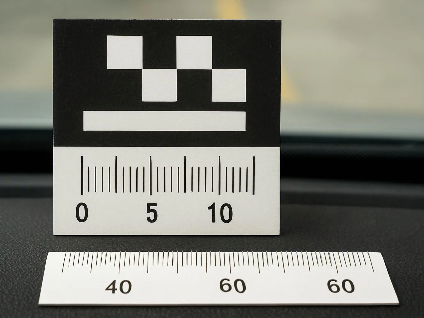 A black-and-white calibration card stands behind a printed ruler strip on a dark surface