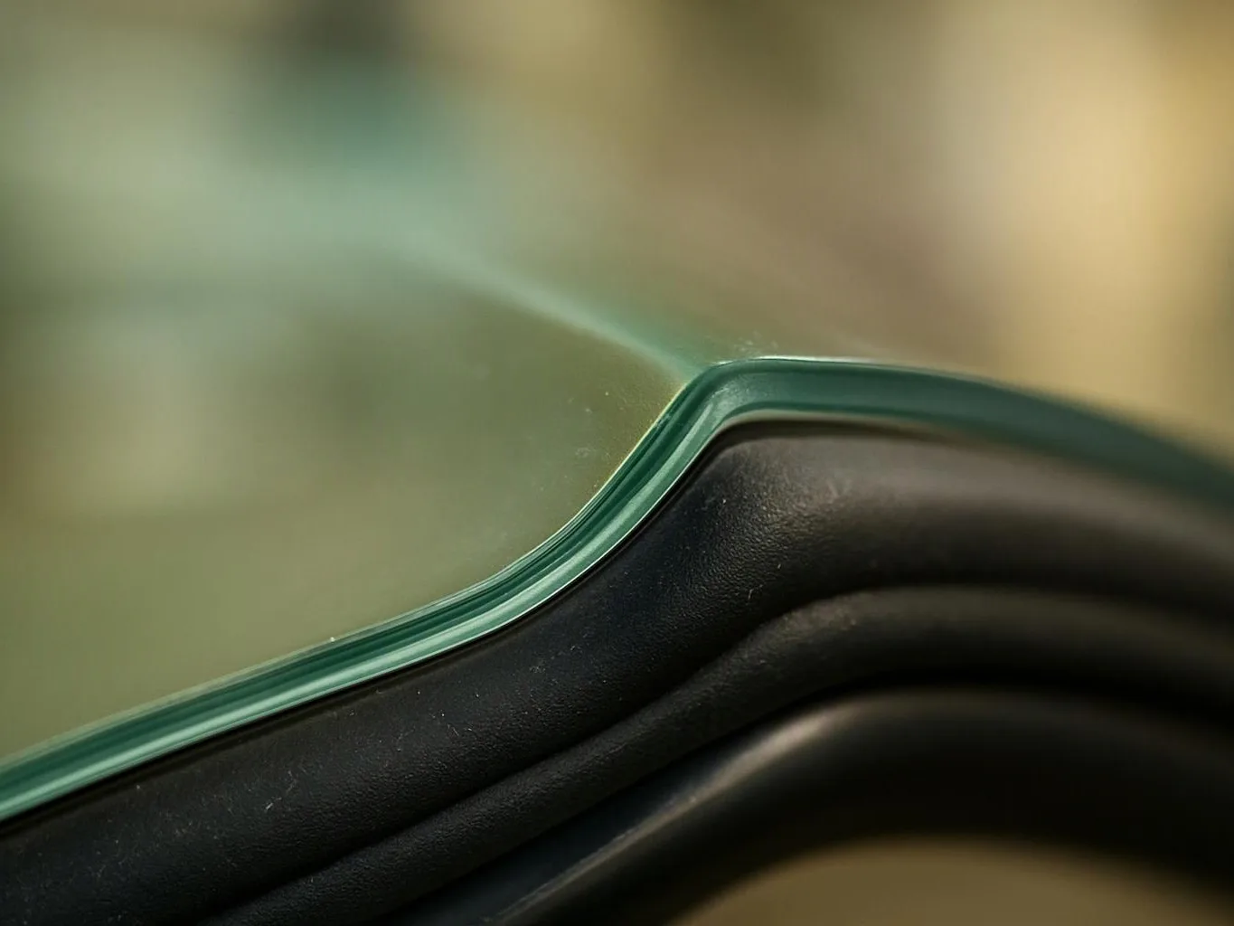 Close-up of a curved green glass edge resting on a black molded surface with a blurred background