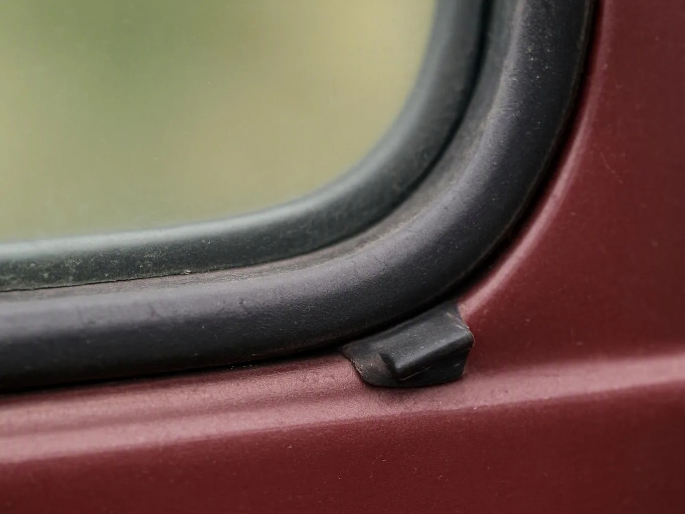 Close-up of a dusty black rubber window seal on a maroon vehicle door