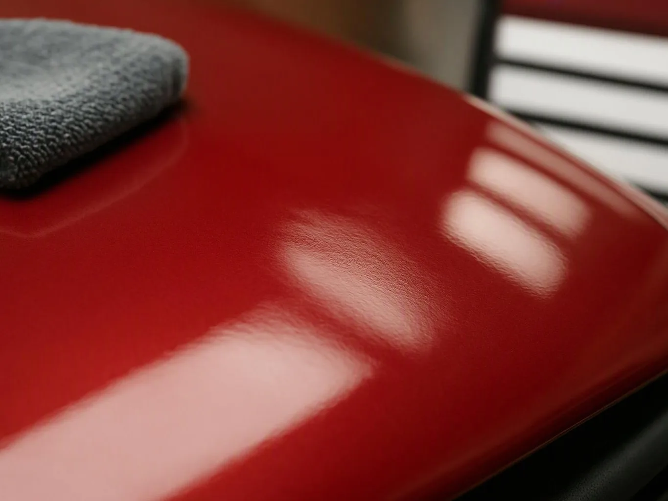 Close-up of a glossy red curved surface with a gray cloth resting on one corner and light reflections