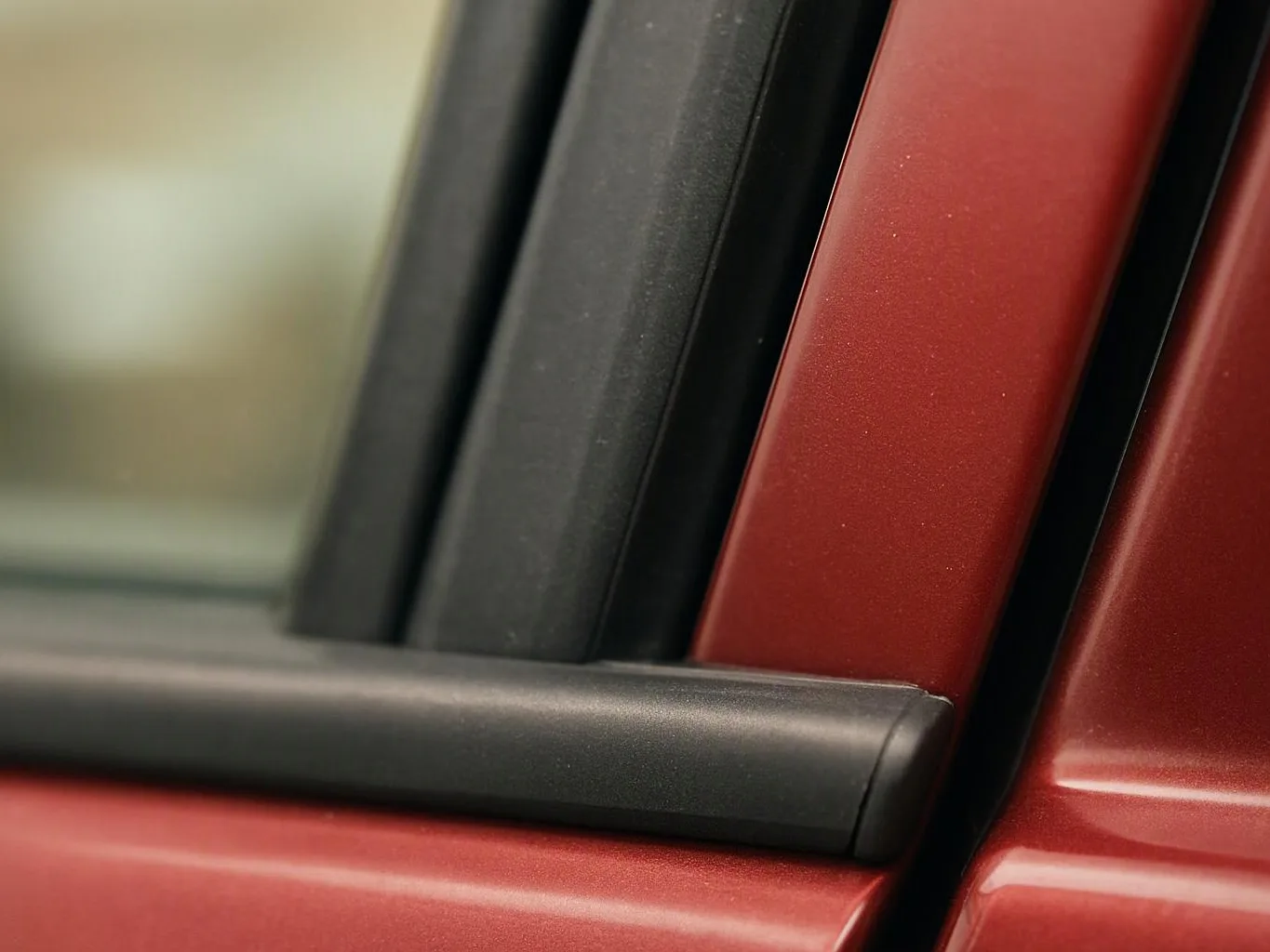 Close-up of a red car door with black trim and a blurred window edge