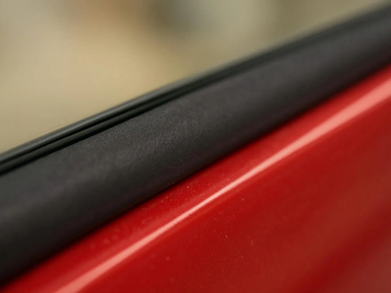 Close-up of a red car door with black window trim and blurred glass above