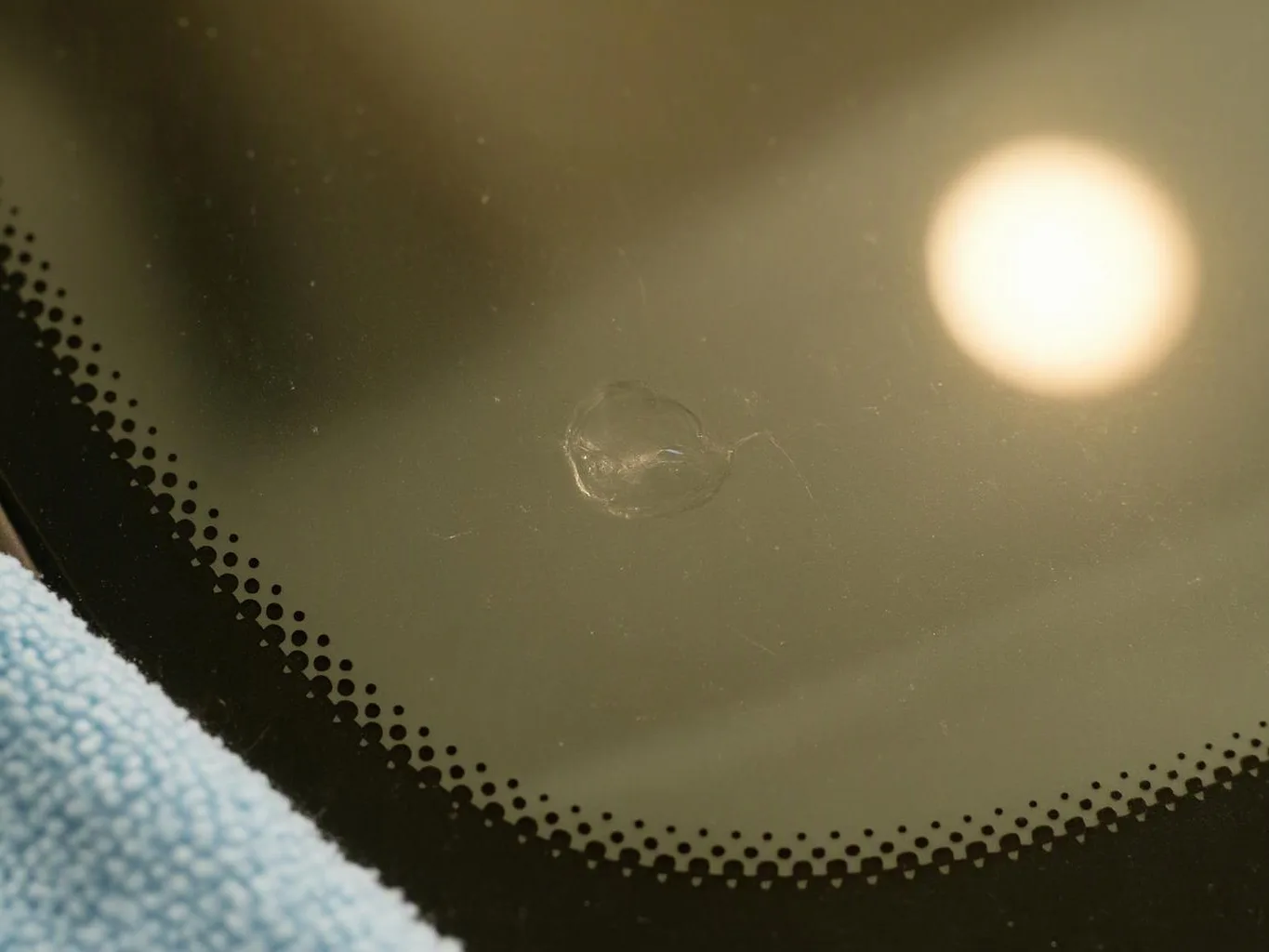 Close-up of a scratched glass lens with a bright reflection and black dotted edge, resting on blue fabric