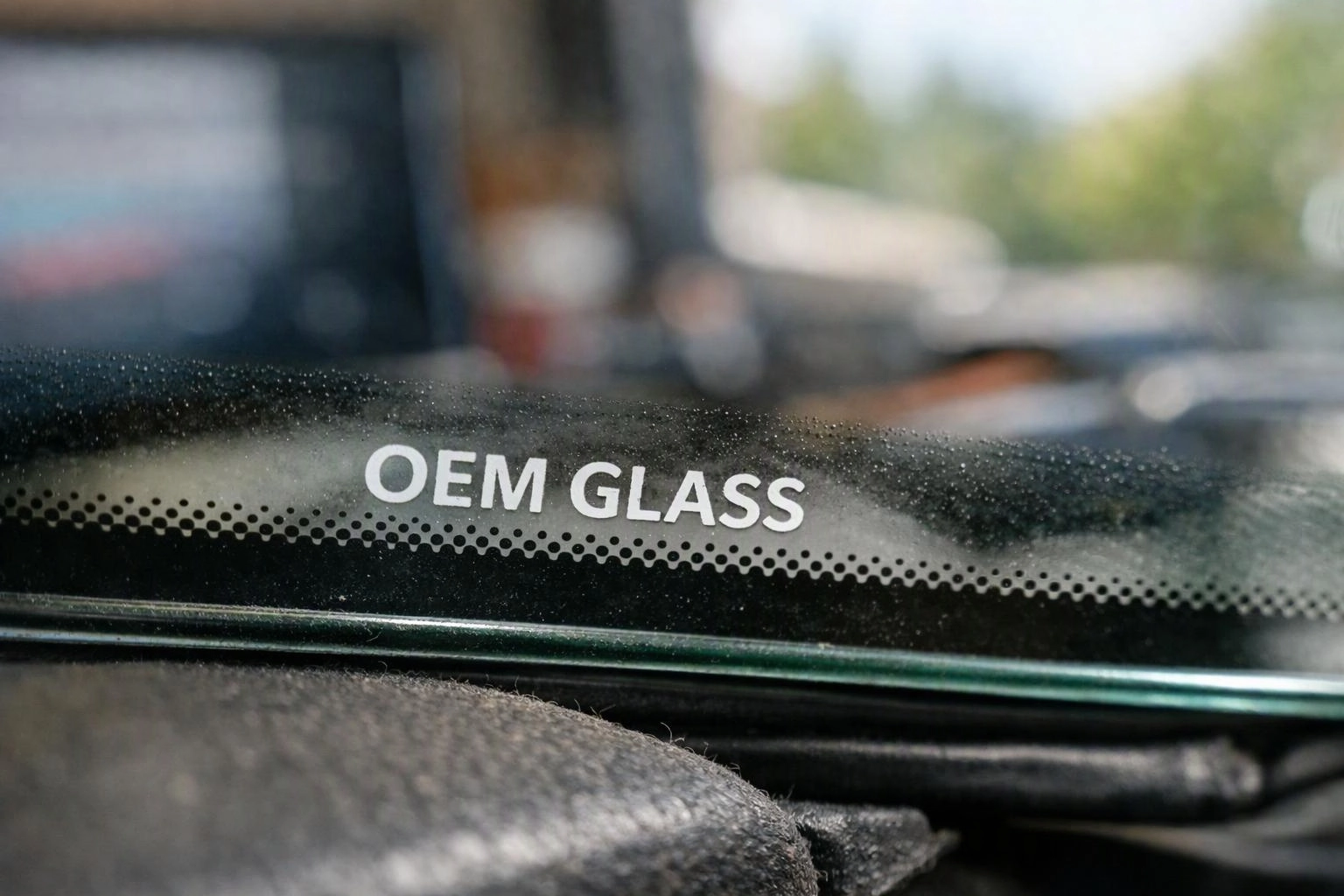 A car windshield shows the words “OEM GLASS” above a dotted black border