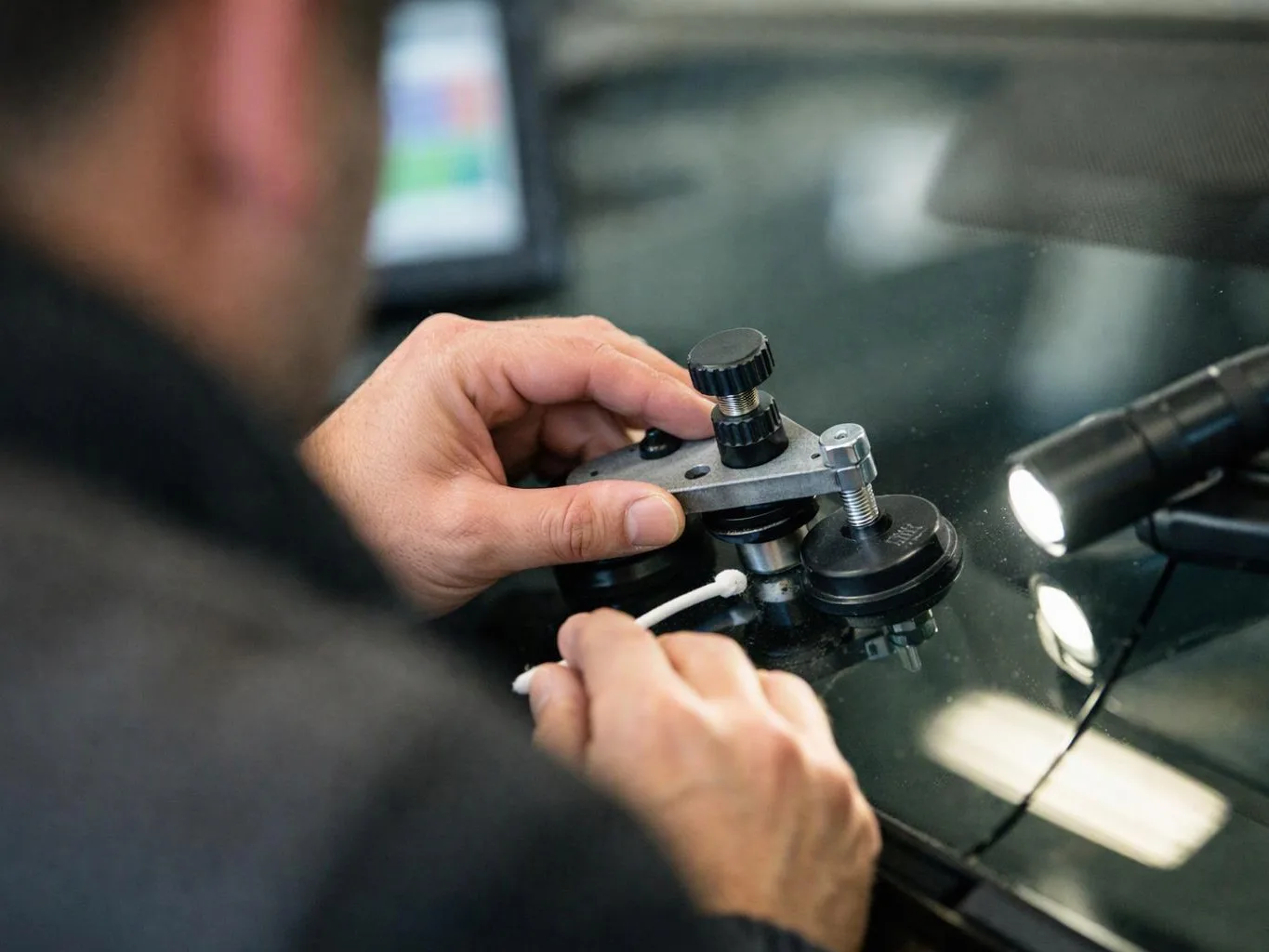 A person adjusts a small mechanical tool on a glossy glass surface with a cotton swab and a flashlight nearby